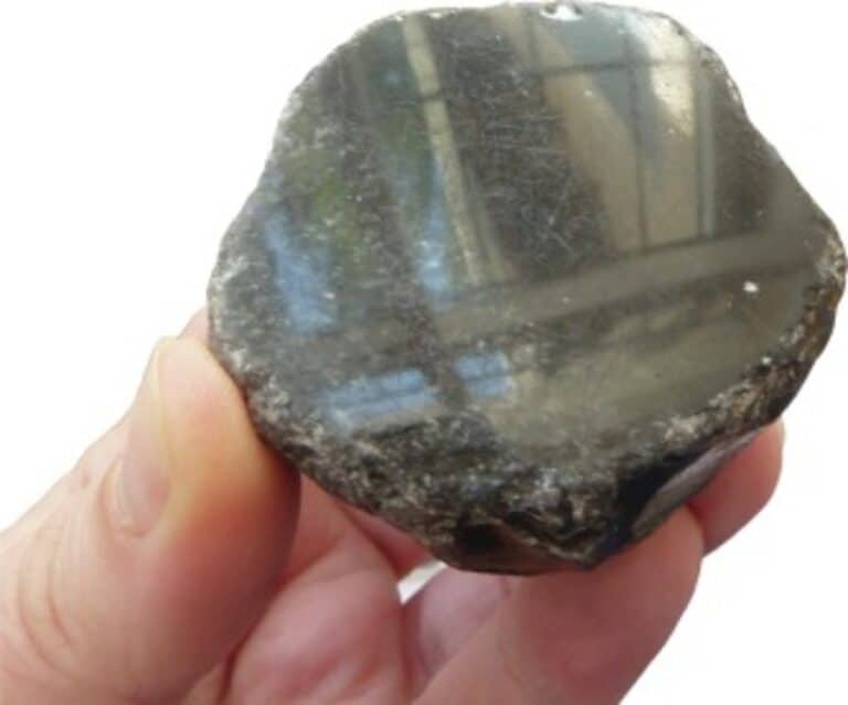 Shiny black mineral pebble with reflective surface, held in hand.